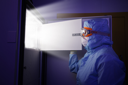 Picture of a person wearing goggles, gloves and a clean suit, opening a freezer shelf