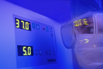 Picture of a person wearing goggles and a clean suit, inspecting the read-out on an incubator